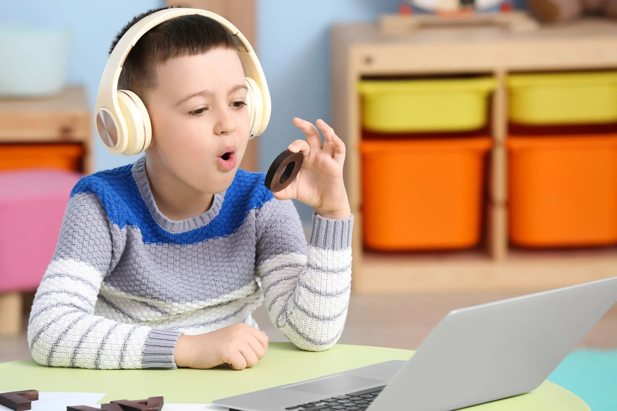 Kleiner Junge mit Notebook-Training spricht Buchstaben O zu Hause aus